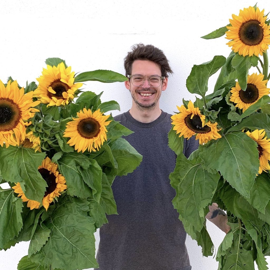 Man smiling and holding large bunches of sunflowers